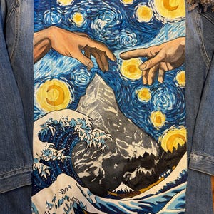 May include: A denim jacket with a painted design on the back. The design features a blue and yellow starry night sky with two hands reaching towards each other, a mountain, and a large wave crashing in the foreground.