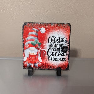 May include: A red and white Christmas gnome holding a mug of hot cocoa with a candy cane. The background is red with white snowflakes and the text "Christmas Candy Canes Cocoa & Cuddles".