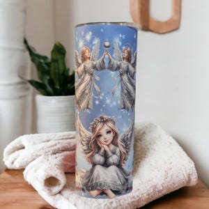 Puede incluir: Un vaso de acero inoxidable con fondo azul y un dise&ntilde;o de &aacute;ngeles sosteniendo una estrella. Los &aacute;ngeles visten vestidos blancos con detalles plateados. El vaso es perfecto para contener bebidas calientes o fr&iacute;as.
