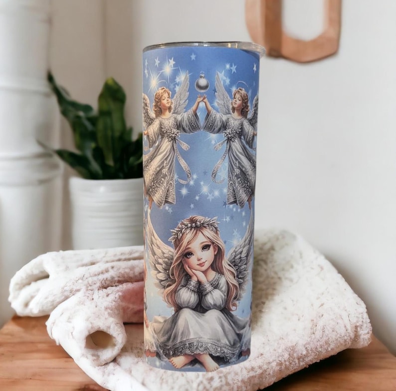 Puede incluir: Un vaso de acero inoxidable con fondo azul y un dise&ntilde;o de &aacute;ngeles sosteniendo una estrella. Los &aacute;ngeles visten vestidos blancos con detalles plateados. El vaso es perfecto para contener bebidas calientes o fr&iacute;as.