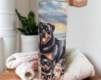 May include: A stainless steel tumbler featuring a Rottweiler dog and puppy on a beach scene with a sunset and birds. The tumbler is cylindrical and has a glossy finish. The design includes black, brown, and tan colors.