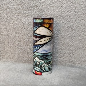 May include: A stainless steel tumbler with a colorful stained glass design featuring blue, green, yellow, and red hues. The design depicts a seascape with waves and clouds.