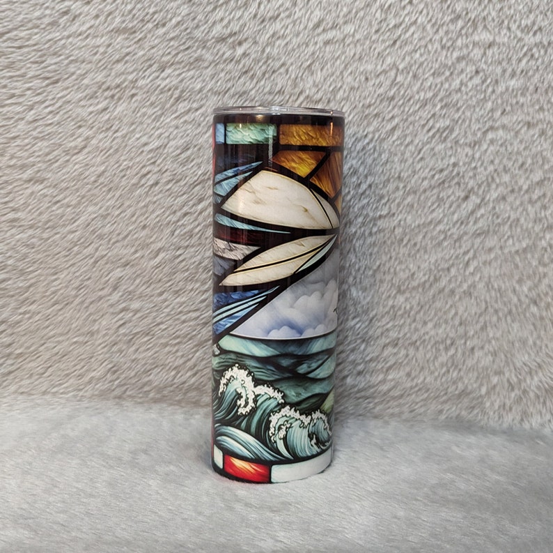 May include: A stainless steel tumbler with a colorful stained glass design featuring blue, green, yellow, and red hues. The design depicts a seascape with waves and clouds.