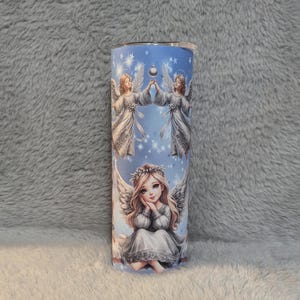 Puede incluir: Un vaso de acero inoxidable con fondo azul y un dise&ntilde;o de tres &aacute;ngeles. Los &aacute;ngeles llevan t&uacute;nicas blancas y tienen halos dorados. El dise&ntilde;o est&aacute; rodeado de estrellas y un patr&oacute;n de espiral azul y blanco.