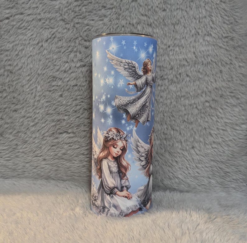 Puede incluir: Un vaso de acero inoxidable con fondo azul y un dise&ntilde;o de tres &aacute;ngeles con alas blancas y vestidos blancos. Los &aacute;ngeles est&aacute;n rodeados de estrellas blancas.