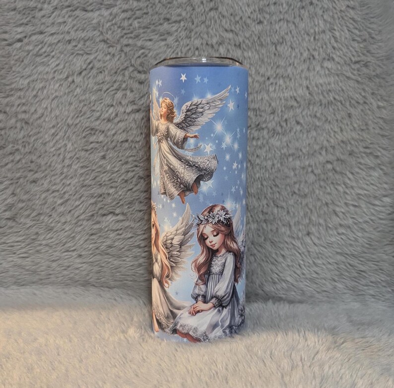 Puede incluir: Un vaso blanco con fondo azul y un dise&ntilde;o de tres &aacute;ngeles con alas. Los &aacute;ngeles est&aacute;n rodeados de estrellas.