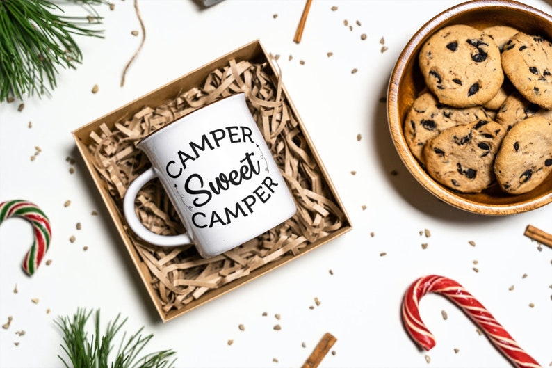 Puede incluir: Taza de cer&aacute;mica blanca con texto negro que dice "Camper, Sweet Camper" en una fuente decorativa. La taza est&aacute; en una caja de regalo de papel marr&oacute;n llena de papel triturado.