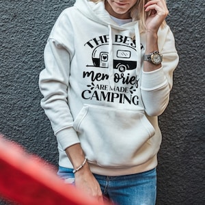 Puede incluir: Sudadera con capucha blanca con un gr&aacute;fico negro que dice "The best memories are made camping" con una ilustraci&oacute;n de una autocaravana.