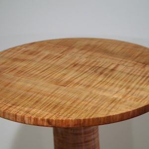 May include: A round wooden table top with a natural wood finish. The table top has a unique grain pattern and is made of solid wood.