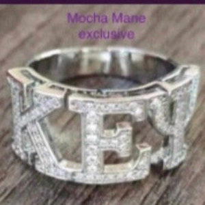 May include: A silver ring with the word "KEY" spelled out in large letters, each letter is encrusted with small clear stones.