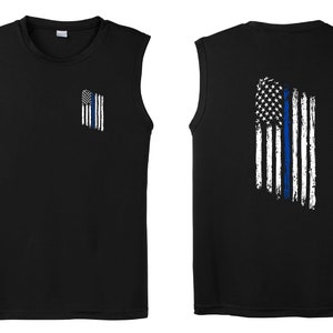 May include: Black sleeveless shirt with a distressed American flag design featuring a blue line down the center. The flag is on the back of the shirt and a smaller version of the flag is on the front of the shirt.