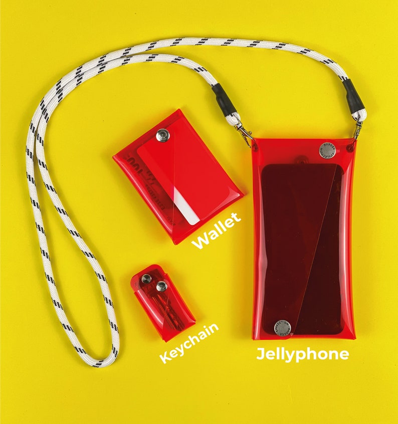 Puede incluir: Una cartera roja, un llavero y una funda transparente para tel&eacute;fono de gel con un cord&oacute;n blanco y negro. Los art&iacute;culos est&aacute;n sobre un fondo amarillo.