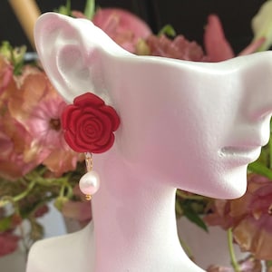 May include: A pair of red rose earrings with a pearl dangle. The earrings are made of polymer clay and have a gold-tone chain.