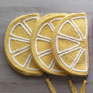 May include: Three crocheted lemon-shaped pouches with white trim and tassels. The pouches are yellow and have a crocheted design that resembles a lemon slice.