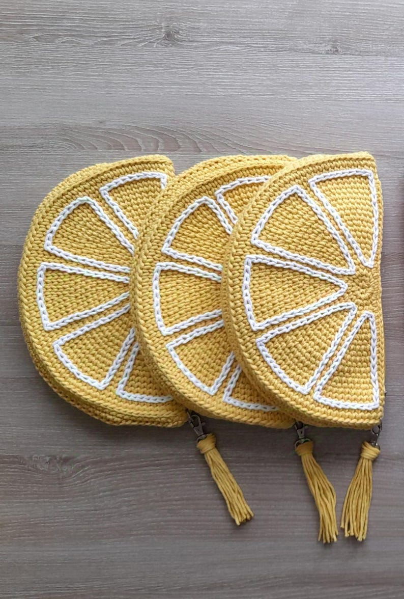 May include: Three crocheted lemon-shaped pouches with white trim and tassels. The pouches are yellow and have a crocheted design that resembles a lemon slice.