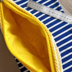 May include: A yellow crocheted zippered pouch with a white tassel. The pouch is lined with yellow fabric and has a zipper closure.
