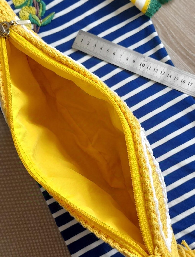 May include: A yellow crocheted zippered pouch with a white tassel. The pouch is lined with yellow fabric and has a zipper closure.