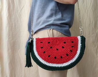 May include: A crocheted watermelon-shaped purse with a silver chain strap and a green tassel. The purse is red, green, and white.