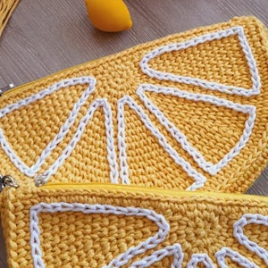 May include: A yellow crocheted lemon-shaped zippered pouch with white stitching. The pouch is open and the zipper is visible.