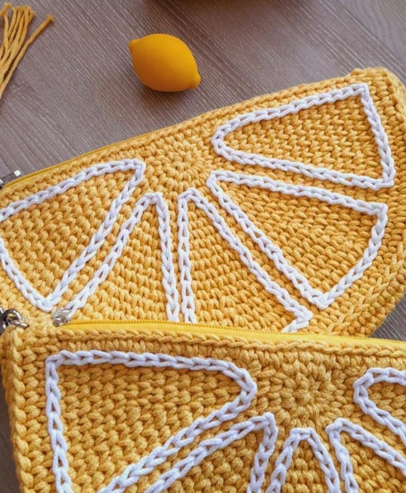 May include: A yellow crocheted lemon-shaped zippered pouch with white stitching. The pouch is open and the zipper is visible.