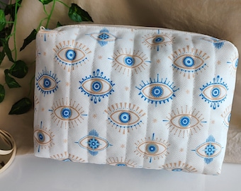 May include: White zippered pouch with a repeating pattern of blue and gold evil eyes.
