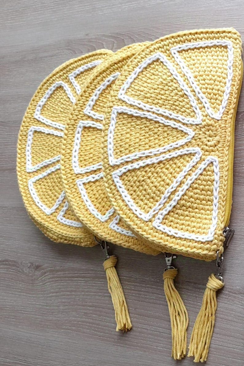 May include: Three crocheted lemon-shaped zippered pouches with yellow and white yarn. Each pouch has a yellow tassel.