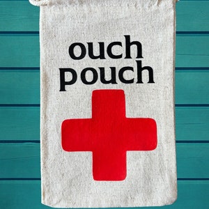 May include: A white canvas pouch with a red cross and the text "ouch pouch" printed on it. The pouch has a drawstring closure and is made of natural fabric.