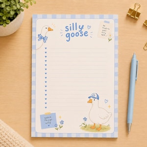 Puede incluir: Un bloc de notas rectangular con un borde de cuadros azul claro, que presenta el texto silly goose en la parte superior. La página incluye líneas horizontales con viñetas en forma de corazón, ilustraciones de gansos y notas que dicen be kind to your silly self y goose things only.