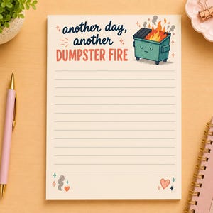 Peut inclure: Un bloc-notes de couleur crème avec des lignes horizontales portant le texte another day, another DUMPSTER FIRE en bleu foncé et orange. Une benne à ordures turquoise avec une expression neutre est en proie aux flammes orange. Des petits cœurs et étincelles décorent le bas.