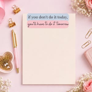May include: A rectangular notepad with a light cream background featuring the text If you don't do it today, you'll have to do it Tomorrow in blue and pink boxes. The notepad is surrounded by a pink pen, gold paper clips, and pink roses.
