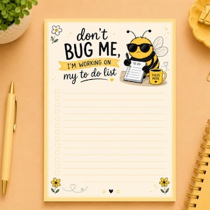 Peut inclure: Un bloc-notes rectangulaire avec un fond crème et une bordure jaune. Le haut présente une abeille dessinée portant des lunettes de soleil, tenant un stylo et un carnet, à côté d'une tasse jaune marquée FOCUS MODE. Le texte indique : don't BUG ME, I'M WORKING ON my to do list.