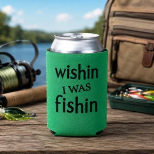 May include: A bright green foam can cooler sleeve featuring the black text "wishin I WAS fishin" printed on the front. The sleeve is cylindrical and designed to hold a standard metal beverage can, providing insulation for the container.