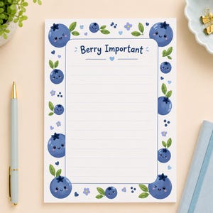 Peut inclure: Un bloc-notes rectangulaire avec des lignes horizontales et une bordure bleue ornée d'illustrations de myrtilles souriantes, de feuilles vertes et de petites fleurs bleues. Le texte Berry Important est imprimé en bleu en haut au centre.