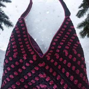 May include: A black and burgundy crochet tote bag with a V-shaped opening. The bag features a dotted pattern in burgundy against a black background. The strap and trim are a darker burgundy color. The interior lining is a solid purple.