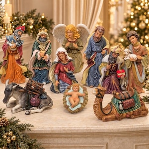 May include: A nativity set featuring figurines of the Holy Family, an angel, three wise men, a donkey, and a camel. The figures are painted in vibrant colors with detailed robes and accessories, arranged on a light-colored surface.