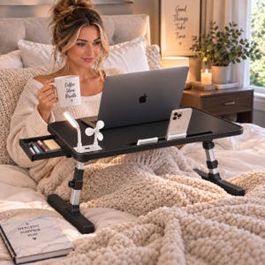 Puede incluir: Un escritorio negro ajustable para portátil con cajón lateral, lámpara LED integrada, ventilador pequeño y soporte para teléfono. El escritorio sostiene un portátil plateado y una taza blanca con el texto Coffee Ideas Results. Un cuaderno con el texto A HEALTHY HAPPIER YOU está cerca.