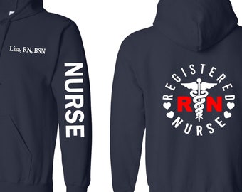 May include: Navy blue zip-up hoodie with white text on the left sleeve that reads "NURSE". The back of the hoodie has a white circle with the text "REGISTERED NURSE" and a red "RN" in the center. The circle also has a white caduceus symbol with two hearts on either side.