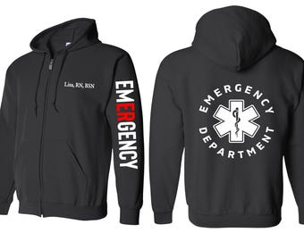 Könnte beinhalten: Schwarzer Kapuzenpullover mit Reißverschluss, mit einem weißen "EMERGENCY DEPARTMENT"-Logo auf der Rückseite und dem Wort "EMERGENCY" in Rot und Weiß auf dem linken Ärmel. Der Hoodie hat ein weißes Textetikett auf der Vorderseite mit der Aufschrift "Lisa, RN, BSN".