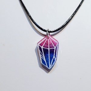 Könnte beinhalten: Eine Halskette mit einem schwarzen Band und einem Anhänger in Form eines Diamanten. Der Diamant ist ein Farbverlauf von Pink, Lila und Blau.