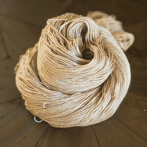 May include: A skein of beige yarn, made from natural fibres, is loosely wound and ready for knitting or crocheting.