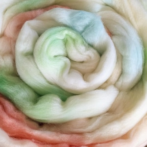 May include: A close-up of a soft, fluffy, multi-colored yarn. The yarn is a gradient of pink, green, and blue.