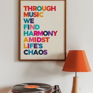 Pu&ograve; includere: Una stampa incorniciata con il testo "THROUGH MUSIC WE FIND HARMONY AMIDST LIFE'S CHAOS" in lettere colorate. La stampa &egrave; appesa a un muro bianco sopra un giradischi e una lampada.
