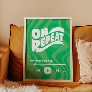 May include: A white framed print with a green background and white text that says "ON REPEAT" in a wavy font. The text "Flux Pavilion and Wooli" is below the main text. A play button and other music player controls are at the bottom of the print.