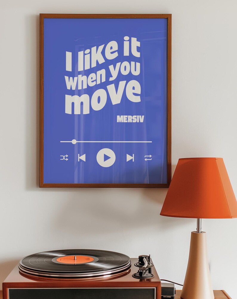 Peut inclure: Une affiche encadr&eacute;e avec un fond bleu et du texte blanc qui dit "J'aime &ccedil;a quand tu bouges" avec le nom de l'artiste "MERSIV" sous le texte. L'affiche a un bouton de lecture et d'autres commandes de lecteur de musique en bas. Un tourne-disque vintage avec un disque noir sur la platine est au premier plan. Une lampe rouge avec une base beige est sur le c&ocirc;t&eacute; droit de l'image.