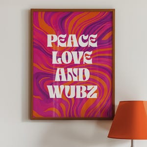 May include: A framed art print with the words "PEACE LOVE AND WUBZ" in white, set against a vibrant, swirling background of pink, orange, and purple. The frame is a warm brown color. An orange lampshade is in the foreground.