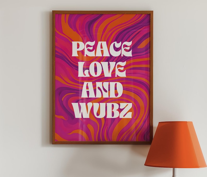 May include: A framed art print with the words "PEACE LOVE AND WUBZ" in white, set against a vibrant, swirling background of pink, orange, and purple. The frame is a warm brown color. An orange lampshade is in the foreground.