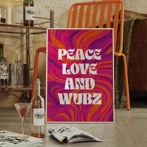 May include: A framed art print with the words "PEACE LOVE AND WUBZ" in white, set against a vibrant, swirling background of orange, pink, and purple. The print is propped up on a wooden floor.