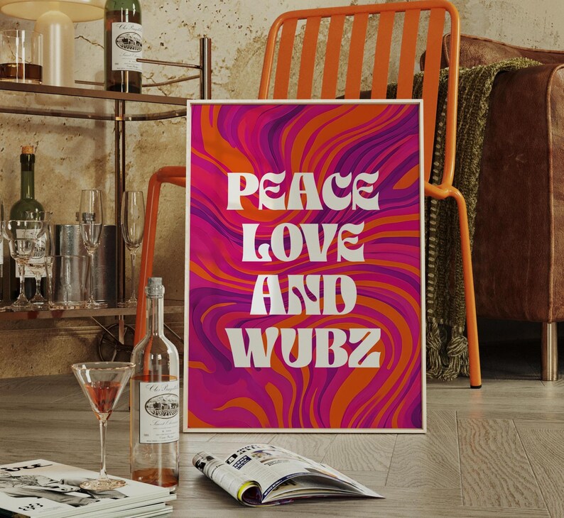 May include: A framed art print with the words "PEACE LOVE AND WUBZ" in white, set against a vibrant, swirling background of orange, pink, and purple. The print is propped up on a wooden floor.