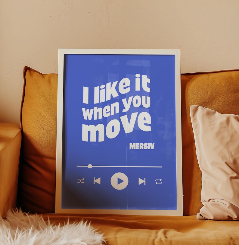 Peut inclure: Une impression encadr&eacute;e bleue avec du texte blanc qui dit "J'aime &ccedil;a quand tu bouges" et le nom de l'artiste "MERSIV" en dessous. L'impression a un bouton de lecture blanc et d'autres commandes de lecteur de musique.