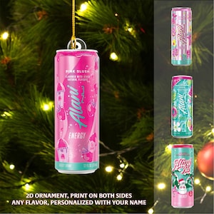 Puede incluir: Un adorno navide&ntilde;o con forma de lata de bebida energ&eacute;tica Alani rosa. La lata lleva la etiqueta "Pink Slush" y "Energy". El adorno cuelga frente a un &aacute;rbol de Navidad. Tambi&eacute;n se muestran latas adicionales con diferentes dise&ntilde;os.